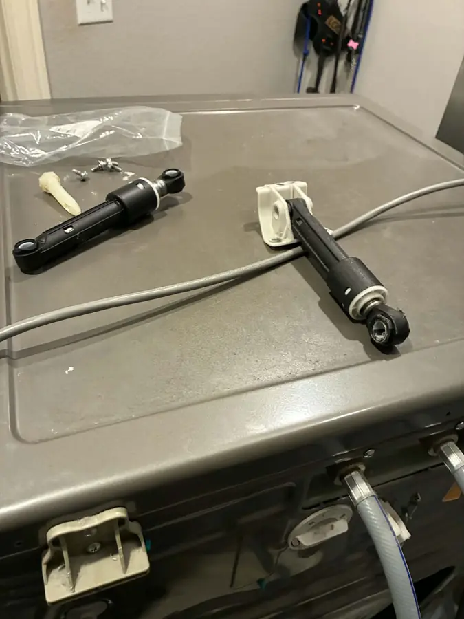 Worn vs. New Washer Dampers: The removed shock absorber next to its replacement, on top of the washer